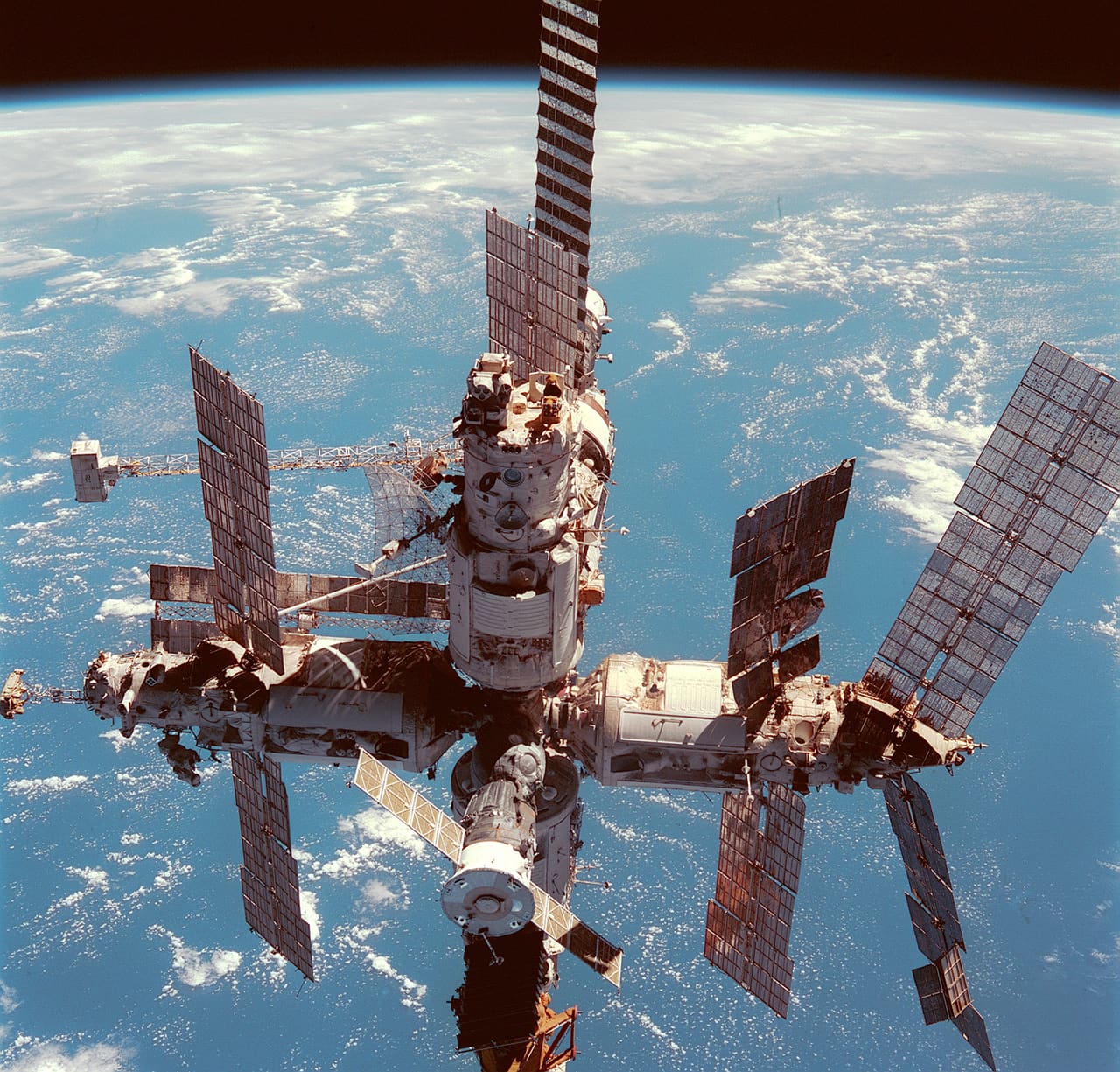 The Mir space station photographed in orbit with its modules and solar arrays against Earth below